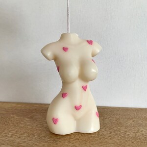 May include: A white candle shaped like a torso with pink hearts on the surface.