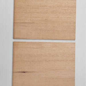 May include: Four rectangular wooden planks with a light brown color and visible wood grain are arranged vertically against a white background. The planks appear to be new and unused.