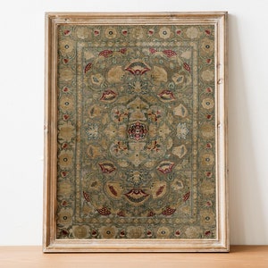 Puede incluir: Una alfombra rectangular enmarcada con un intrincado diseño floral en tonos verde oliva, rojo y beige. La alfombra se exhibe en un marco de madera clara y envejecida. El diseño presenta un medallón central y bordes detallados.