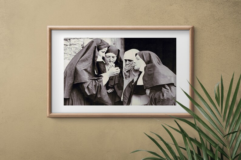 May include: A black and white photograph of four nuns standing together, each holding a cigarette. The nuns are wearing traditional habits, and the photo is framed in a wooden frame.