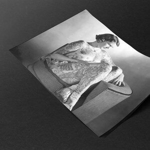 Puede incluir: Una fotograf&iacute;a en blanco y negro de una persona sentada en una silla. La persona est&aacute; cubierta de tatuajes. Los tatuajes son intrincados y detallados, y cubren todo el cuerpo de la persona.