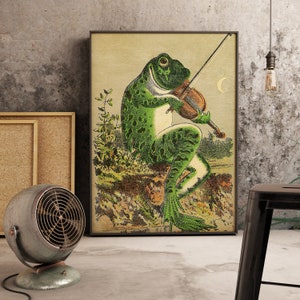 May include: A green frog playing a violin with a crescent moon in the background. The frog is sitting on a rock with green leaves and flowers around it.