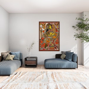 May include: A framed painting of a colorful Indian folk art scene depicting a couple in traditional clothing. The painting is set against a white wall in a modern living room with a blue couch and a potted plant.