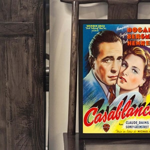 May include: A framed movie poster for "Casablanca" featuring Humphrey Bogart and Ingrid Bergman. The poster has a yellow and blue background with the film's title in red. The actors' names and the Warner Bros. logo are also visible.