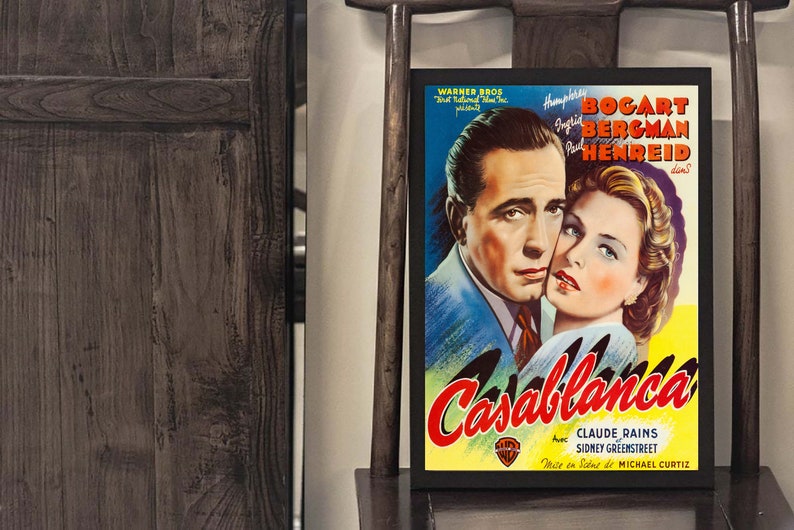 May include: A framed movie poster for "Casablanca" featuring Humphrey Bogart and Ingrid Bergman. The poster has a yellow and blue background with the film's title in red. The actors' names and the Warner Bros. logo are also visible.