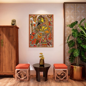 May include: A living room interior design with a wooden cabinet, two orange cushioned stools, a round black table, and two potted plants with gold pots. A framed painting with a colorful design hangs on the wall.