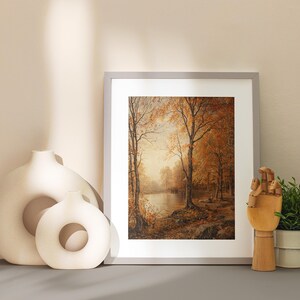 May include: A framed print of a painting depicting a forest scene with trees in shades of brown and yellow. The trees are reflected in a still body of water in the foreground. The print is displayed on a light beige surface with two white ceramic vases.