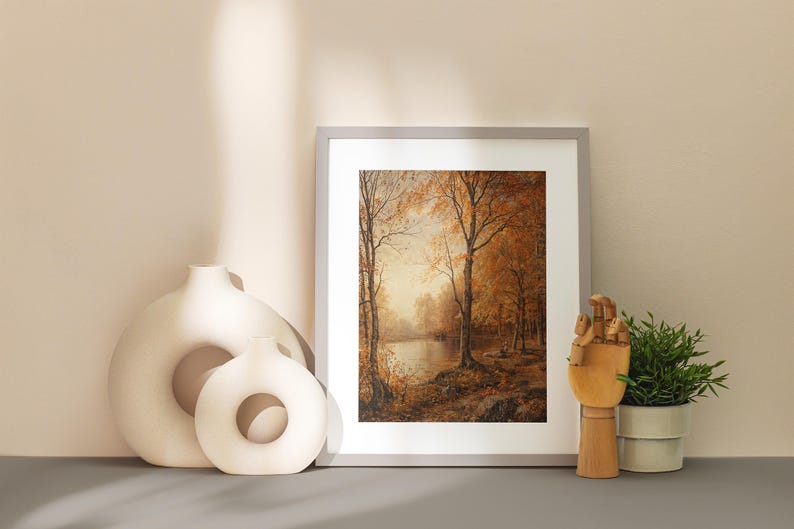 May include: A framed print of a painting depicting a forest scene with trees in shades of brown and yellow. The trees are reflected in a still body of water in the foreground. The print is displayed on a light beige surface with two white ceramic vases.