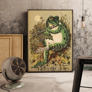 May include: A vintage illustration of a green frog playing a flute in a woodland setting. The frog is perched on a rock and surrounded by flowers and foliage. The illustration is presented in a black frame.