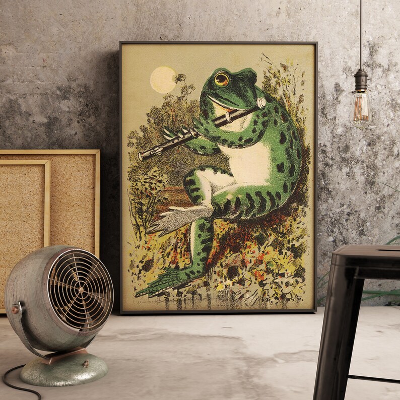 May include: A vintage illustration of a green frog playing a flute in a woodland setting. The frog is perched on a rock and surrounded by flowers and foliage. The illustration is presented in a black frame.