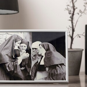 May include: Black and white photograph of four nuns in habits smoking cigarettes. The photo is framed in a silver frame and displayed on a table.