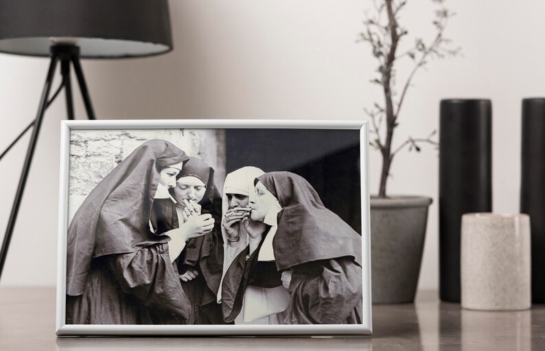 May include: Black and white photograph of four nuns in habits smoking cigarettes. The photo is framed in a silver frame and displayed on a table.