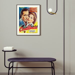 May include: A room interior featuring a framed "Casablanca" movie poster, a black bench with a side table, and a modern black floor lamp with globe lights. The bench has a dark purple seat.