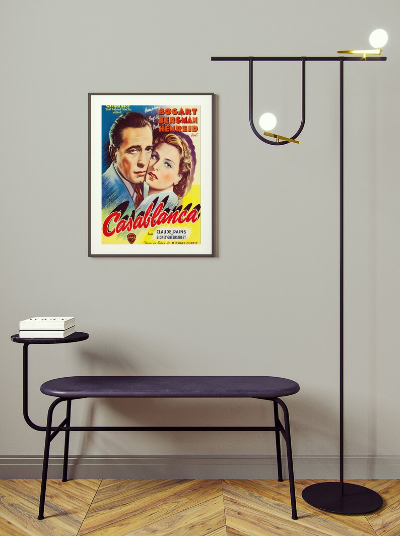 May include: A room interior featuring a framed "Casablanca" movie poster, a black bench with a side table, and a modern black floor lamp with globe lights. The bench has a dark purple seat.