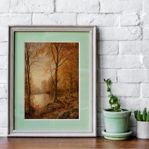 May include: A framed painting of a forest scene with trees in autumn colors, a lake, and a light blue sky. The frame is a light gray color with a light green mat.