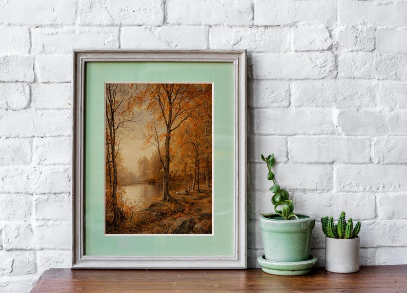 May include: A framed painting of a forest scene with trees in autumn colors, a lake, and a light blue sky. The frame is a light gray color with a light green mat.
