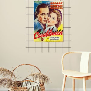 May include: A framed vintage movie poster for "Casablanca" featuring Humphrey Bogart and Ingrid Bergman. The poster has a yellow and red title with the names of the actors and director. The poster is hanging on a grid.