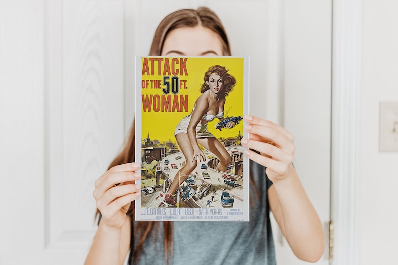 K&ouml;nnte beinhalten: Ein Vintage-Filmplakat f&uuml;r den Film "Attack of the 50 Ft. Woman". Das Plakat zeigt eine Frau in einem wei&szlig;en Kleid und roten Schuhen, die auf einer Autobahn steht und &uuml;ber Autos und Geb&auml;ude ragt. Das Plakat ist gelb mit rotem und schwarzem Text.