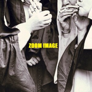 May include: A black and white photo of three people wearing long robes, two of whom are smoking cigarettes. The photo is captioned "ZOOM IMAGE".