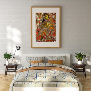 May include: A framed artwork depicting a colorful Indian folk painting with a couple in the center. The painting is set against a white brick wall, above a white bed with a blue and white patterned duvet and a brown throw blanket.