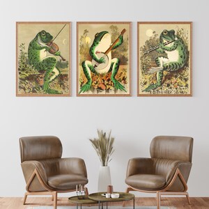 May include: Three framed illustrations of frogs playing musical instruments. The first frog plays a violin, the second plays a banjo, and the third plays a flute. The illustrations are in a vintage style with a green, brown, and yellow colour scheme.