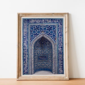 Può includere: Una stampa incorniciata di un arco in piastrelle blu e bianche con motivi intricati e scrittura araba. L'arco è incorniciato in una cornice di legno chiaro.