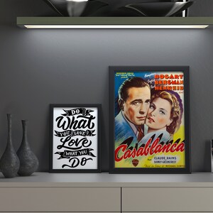 May include: A display featuring framed art and decorative items. A framed poster of the movie "Casablanca" is next to a framed print with the text "Do What You Love". A black clock and vases complete the arrangement.