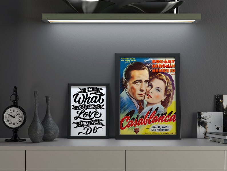 May include: A display featuring framed art and decorative items. A framed poster of the movie "Casablanca" is next to a framed print with the text "Do What You Love". A black clock and vases complete the arrangement.