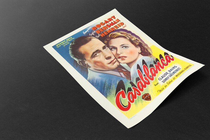 May include: A vintage movie poster for the film "Casablanca" featuring Humphrey Bogart and Ingrid Bergman. The poster has a colorful design with the film's title in red and yellow, and the Warner Bros. logo.