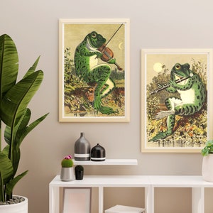 May include: Two framed illustrations of frogs playing musical instruments. The frog on the left is playing a violin and the frog on the right is playing a flute.