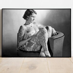 Puede incluir: Fotograf&iacute;a en blanco y negro de una mujer con tatuajes que cubren todo su cuerpo. Est&aacute; sentada en una silla con las piernas cruzadas y mirando hacia abajo.