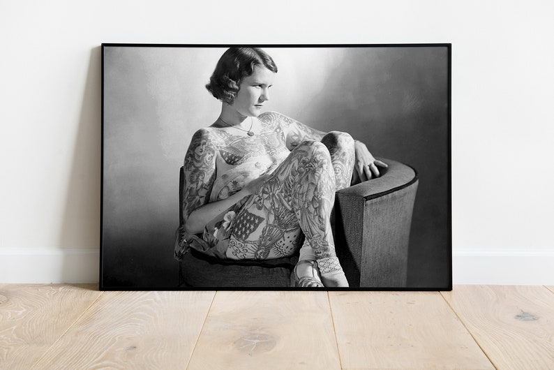 Puede incluir: Fotograf&iacute;a en blanco y negro de una mujer con tatuajes que cubren todo su cuerpo. Est&aacute; sentada en una silla con las piernas cruzadas y mirando hacia abajo.