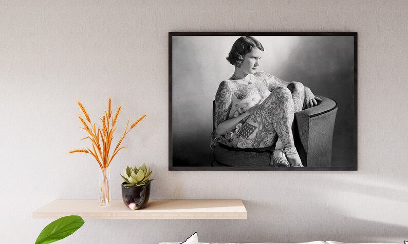 Puede incluir: Fotograf&iacute;a en blanco y negro de una mujer con tatuajes que cubren todo su cuerpo, sentada en una silla. Ella est&aacute; mirando hacia abajo y hacia la derecha.