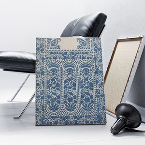 Puede incluir: Una impresi&oacute;n en lienzo con estampado azul y blanco con un dise&ntilde;o floral. La impresi&oacute;n se apoya en una silla de cuero negro y un marco blanco.