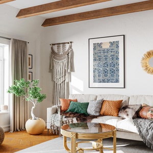 Puede incluir: Una sala de estar con un sof&aacute; blanco, una mesa de centro, un puf tejido, una planta en maceta y un tapiz de pared. El sof&aacute; tiene una variedad de almohadas en diferentes colores y texturas. La mesa de centro est&aacute; hecha de madera y tiene una tapa de vidrio. El puf est&aacute; hecho de mimbre tejido. La planta es un &aacute;rbol peque&ntilde;o con hojas verdes. El tapiz est&aacute; hecho de macram&eacute; y tiene flecos.