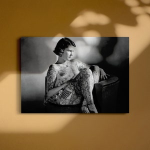 Puede incluir: Una fotograf&iacute;a en blanco y negro de una mujer sentada en una silla. Lleva una camisa de manga corta y tiene tatuajes en los brazos y las piernas.