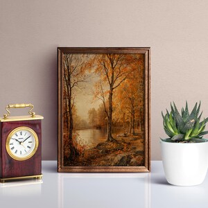 May include: A framed painting of a forest scene with a lake in the background. The trees are in autumn colors of yellow, orange, and red. The lake is calm and reflective. The painting is in a brown frame.