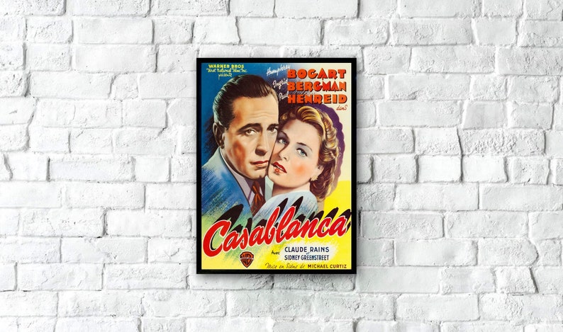 May include: A framed vintage movie poster for "Casablanca" featuring Humphrey Bogart and Ingrid Bergman. The poster has a blue, yellow, and red color scheme with the film's title prominently displayed. The poster is mounted on a white brick wall.