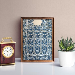 Puede incluir: Una impresi&oacute;n enmarcada de un patr&oacute;n floral azul y blanco con un borde decorativo. La impresi&oacute;n est&aacute; colgada en una pared marr&oacute;n claro, junto a un peque&ntilde;o reloj y una suculenta en maceta.