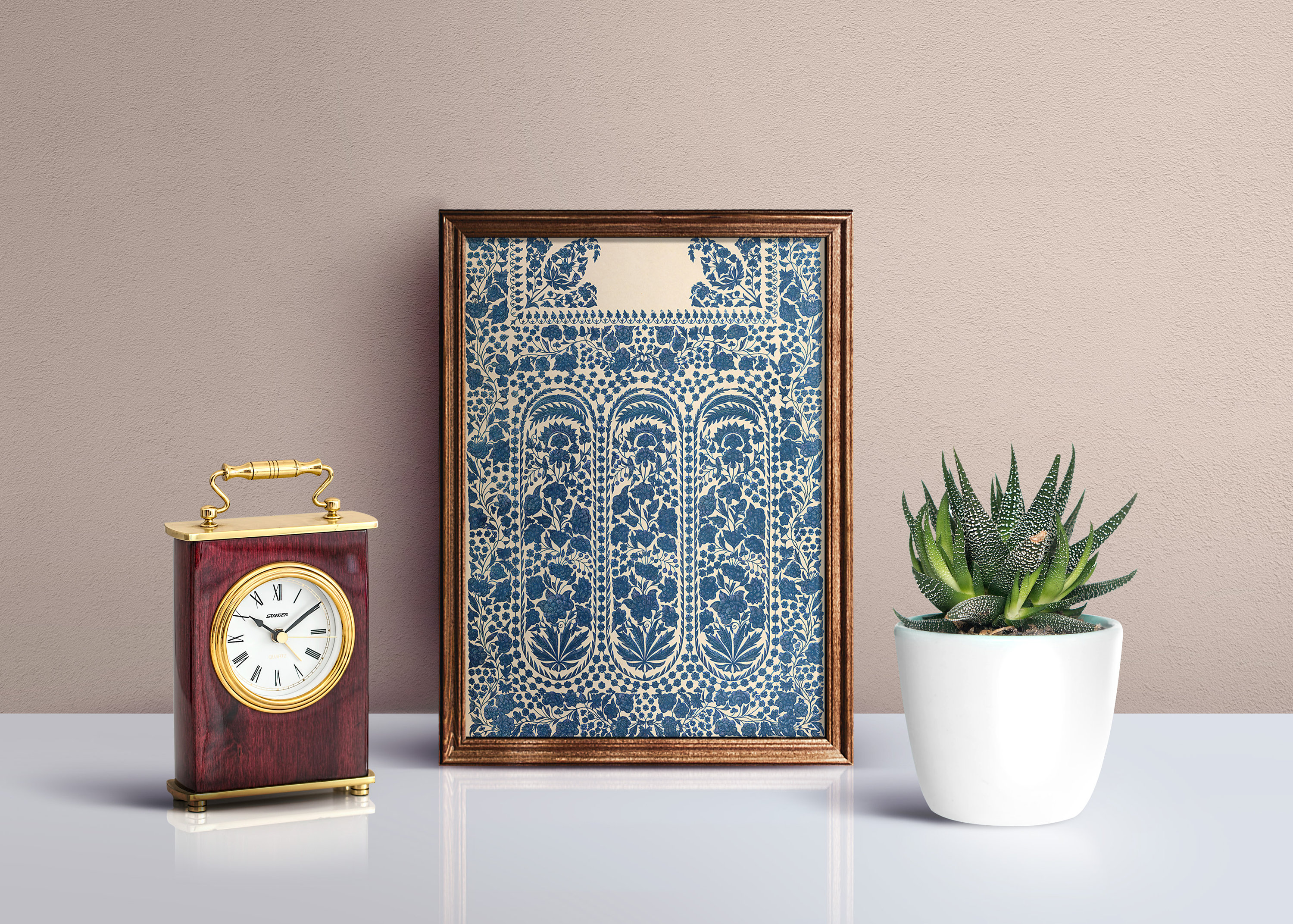 Puede incluir: Una impresi&oacute;n enmarcada de un patr&oacute;n floral azul y blanco con un borde decorativo. La impresi&oacute;n est&aacute; colgada en una pared marr&oacute;n claro, junto a un peque&ntilde;o reloj y una suculenta en maceta.