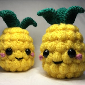 May include: Two crocheted pineapple plushies with smiling faces and pink cheeks. The pineapples are yellow with green leaves.
