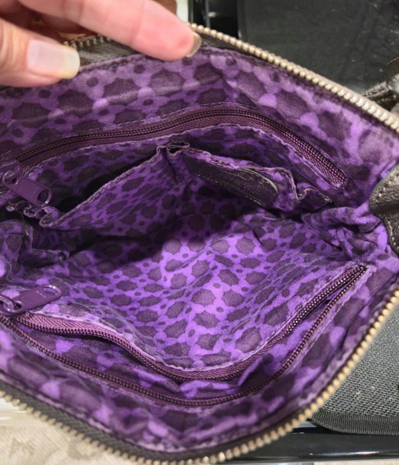 K&ouml;nnte beinhalten: Innenansicht einer braunen Umh&auml;ngetasche mit lila Leopardenmuster-Futter. Die Tasche hat mehrere F&auml;cher und einen Rei&szlig;verschluss. Der Innenraum ist leuchtend lila mit einem dunkleren Leopardenmuster.