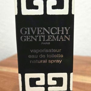 May include: A rectangular Givenchy Gentleman eau de toilette natural spray box in black and white. The top and bottom feature a repeating white geometric logo pattern on a black background. Text reads GIVENCHY GENTLEMAN PARIS vaporisateur eau de toilette natural spray 30 ml 1 FL.OZ.