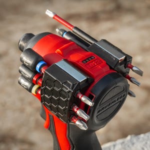 May include: A red and black cordless impact driver with multiple attached bits. The tool has a black handle and a black and gray accessory holder. The brand name "M12" is visible on the tool.