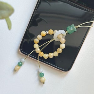 May include: A yellow and white beaded bracelet with a green jade pendant and a white jade ring. The bracelet is tied with a green string and has a green and white bead tassel.