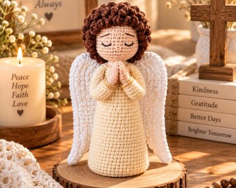 May include: A crocheted angel figurine with curly brown hair, a pale yellow dress, and white wings. The angel has closed eyes and hands pressed together in a prayer position. The figure is crafted with detailed yarn stitching and stands upright.
