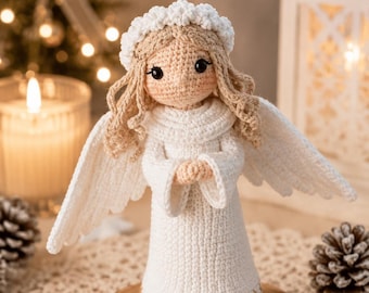 May include: A crocheted angel doll with light beige yarn hair, a white halo, and white wings. The doll wears a long white dress with a subtle gold embroidered hemline, black bead eyes, and has its hands clasped together in a prayer-like position.