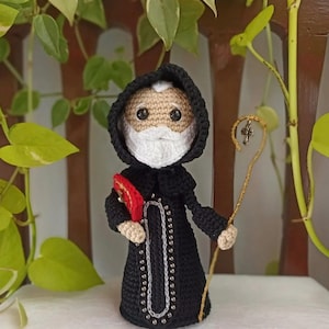 May include: Crocheted amigurumi doll of a religious figure wearing a black robe with a white beard and a red and gold staff.
