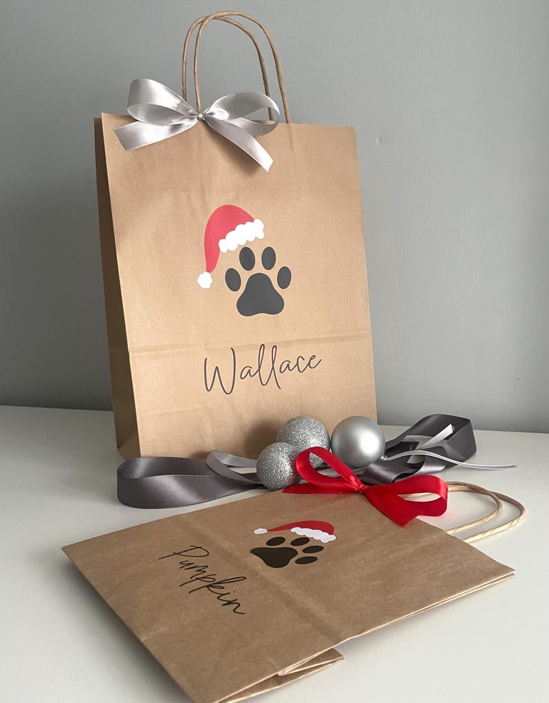 May include: Two brown paper gift bags with a paw print design and a Santa hat. The bags are personalized with the names "Wallace" and "Pumpkin".