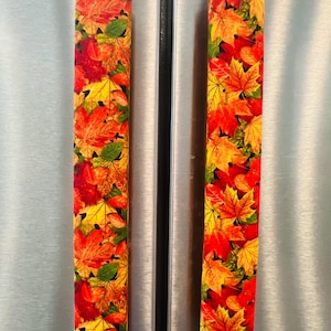 May include: Two refrigerator handle covers with a vibrant autumn leaf pattern. The covers feature red, orange, yellow, and green leaves, creating a seasonal and decorative touch. The covers are rectangular and designed to fit over refrigerator handles.